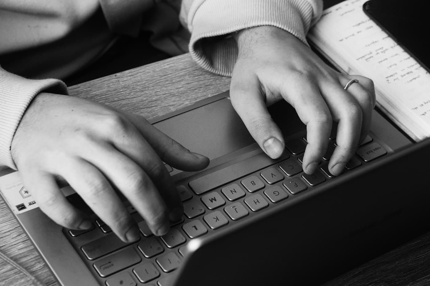 Hands typing on a laptop next to an open notebook with a handwritten list